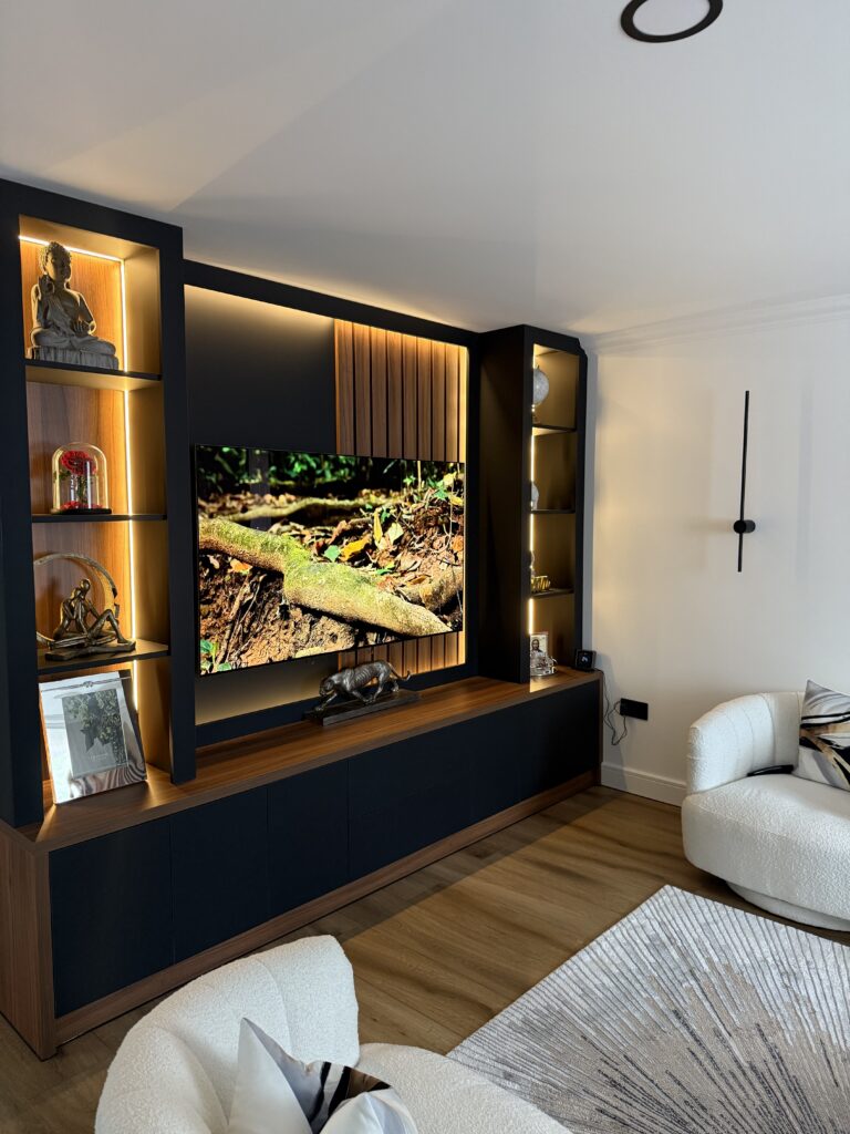 Completed bespoke media wall with illuminated walnut shelving and concealed storage