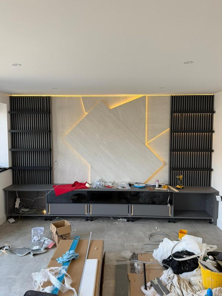 Bespoke media wall during installation featuring integrated LED lighting, floating cabinets and decorative slatted wall panels in a Hertfordshire summer house