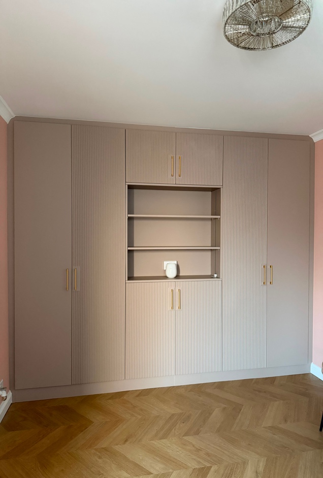 Completed floor-to-ceiling fitted wardrobe in Milton Keynes with Almond Beige fluted doors, gold handles and central open shelving